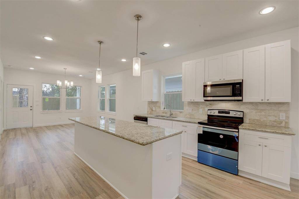 Experience a bright, modern kitchen with an open layout, featuring sleek white cabinetry, granite countertops, and stainless steel appliances. Enhanced by recessed and pendant lighting, the space is beautifully complemented by light vinyl wood flooring.