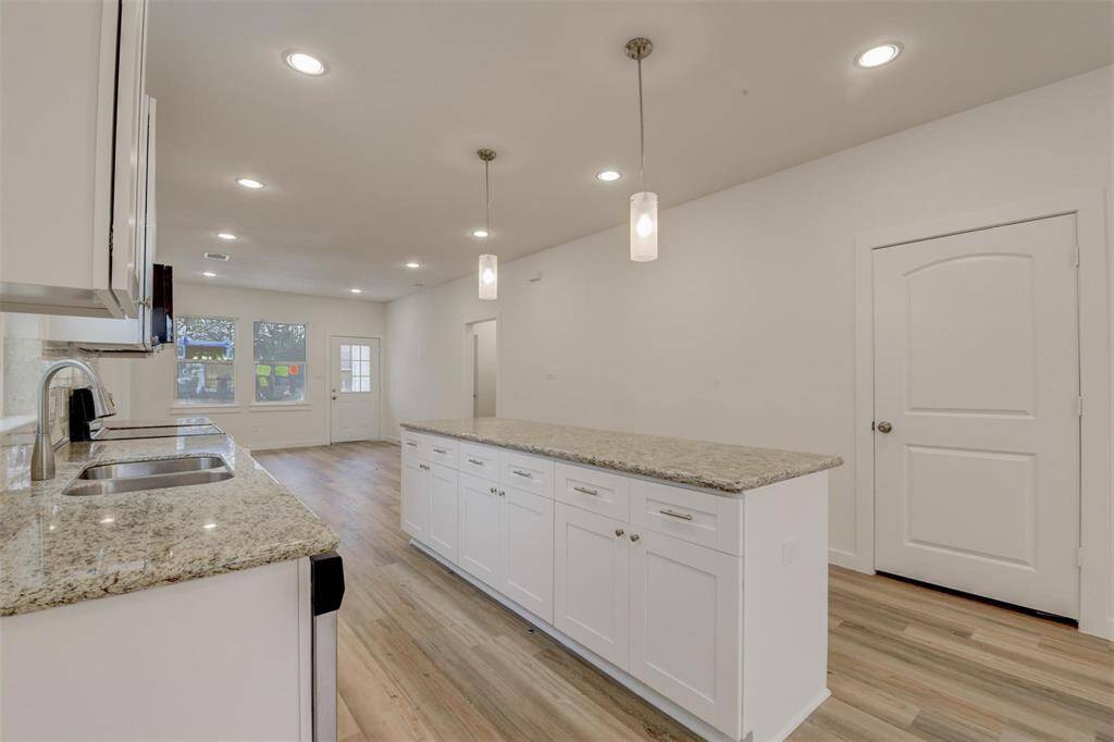 Discover a sleek, modern kitchen featuring an open layout, granite countertops, and elegant white cabinetry. Wood laminate flooring and stylish lighting create a bright, inviting space.