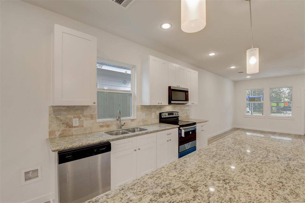 Sleek kitchen with granite countertops, stainless steel appliances, and bright white cabinetry. Enjoy an open layout with stylish pendant lighting and abundant natural light from large windows.