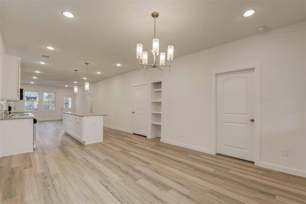 Discover this inviting open-concept living space featuring light wood floors and modern lighting. The kitchen boasts a granite island and sleek white cabinets, flowing into a bright dining area bathed in natural light from large windows.