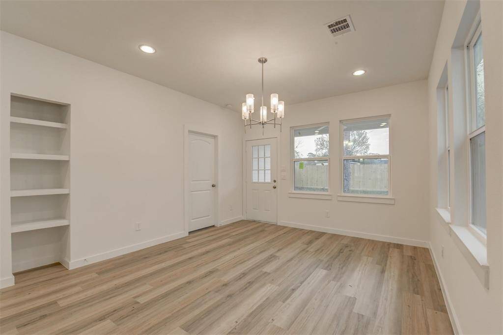 Bright and inviting room with large windows, recessed lighting, and a modern chandelier. Features built-in shelves and stylish wood-look flooring, ideal for dining or living space.