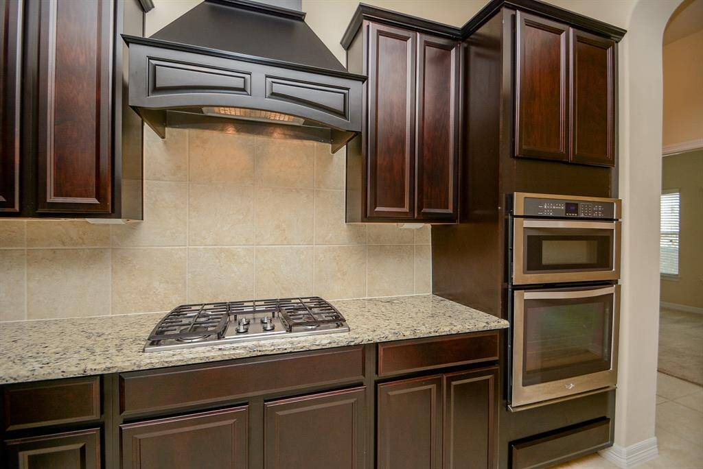A gorgeous, rustic exhaust over the built in range top, adds purpose and beauty! Granite countertops surround these appointments, with a creamy, tile backsplash.