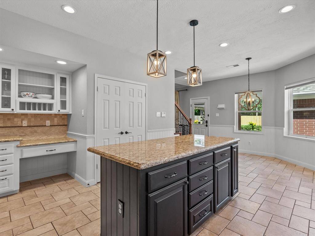 This kitchen features a spacious island with granite countertops and dark cabinetry, complemented by modern pendant lighting.