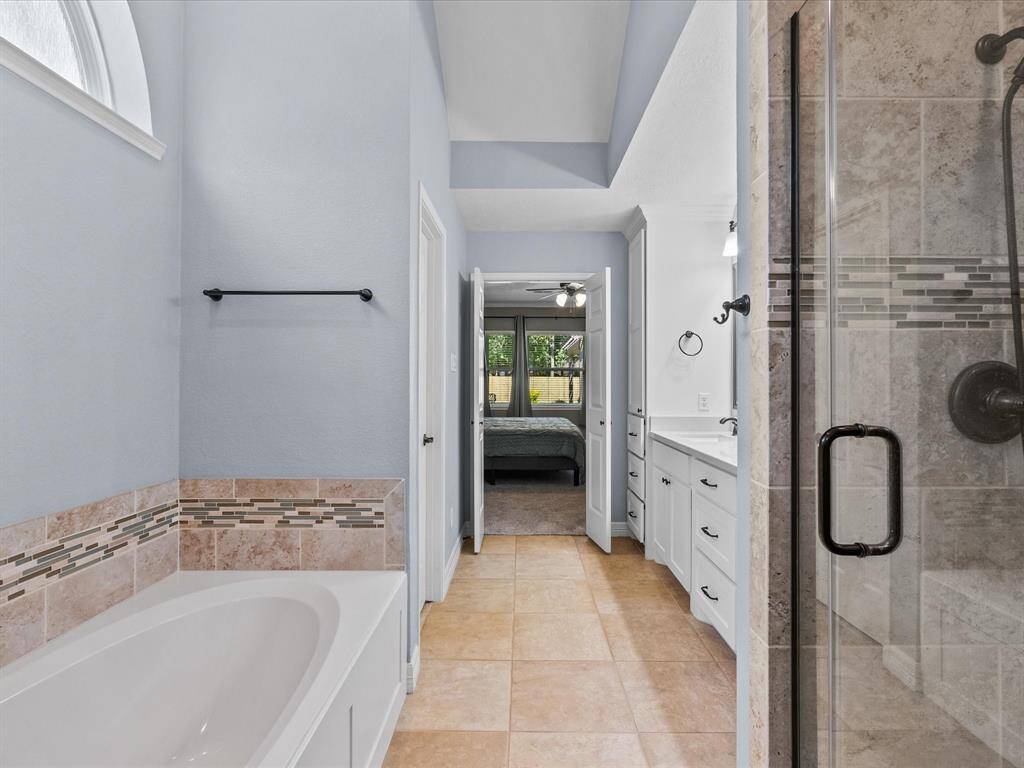 This bathroom features a spacious design with a large bathtub, glass-enclosed shower, and double vanity.