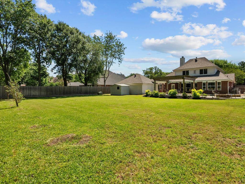 Spacious backyard featuring a well-maintained lawn, mature trees, a garden shed, and a covered patio. Perfect for outdoor activities and relaxation.