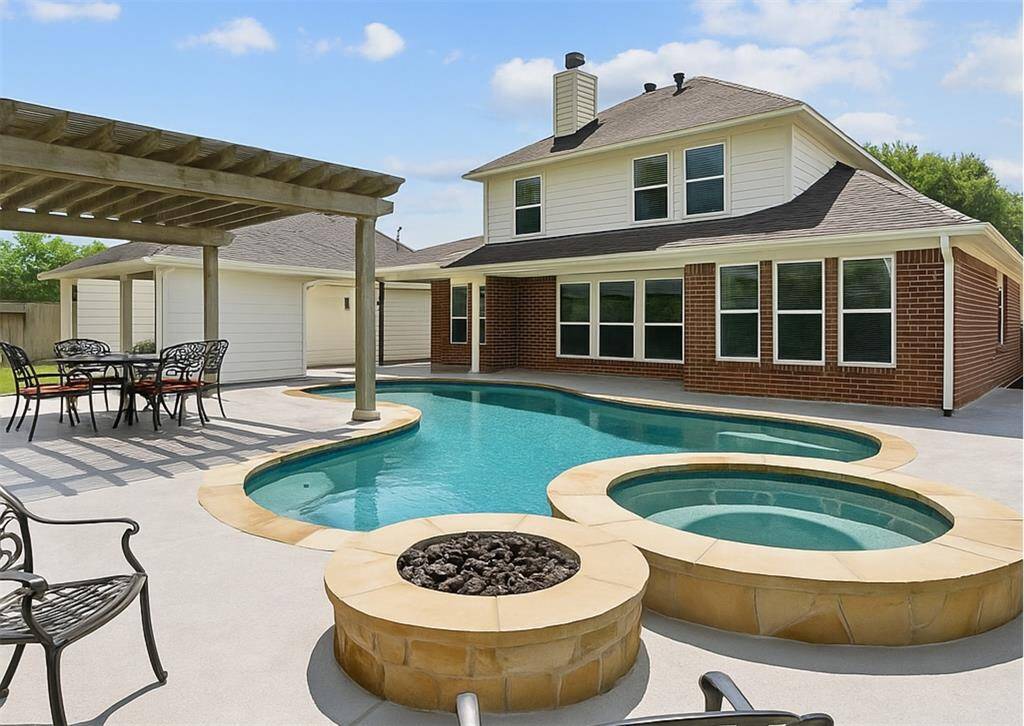 Spacious covered patio overlooking the pool and hot tub, with a pergola and landscaped yard providing a private, relaxing outdoor space.