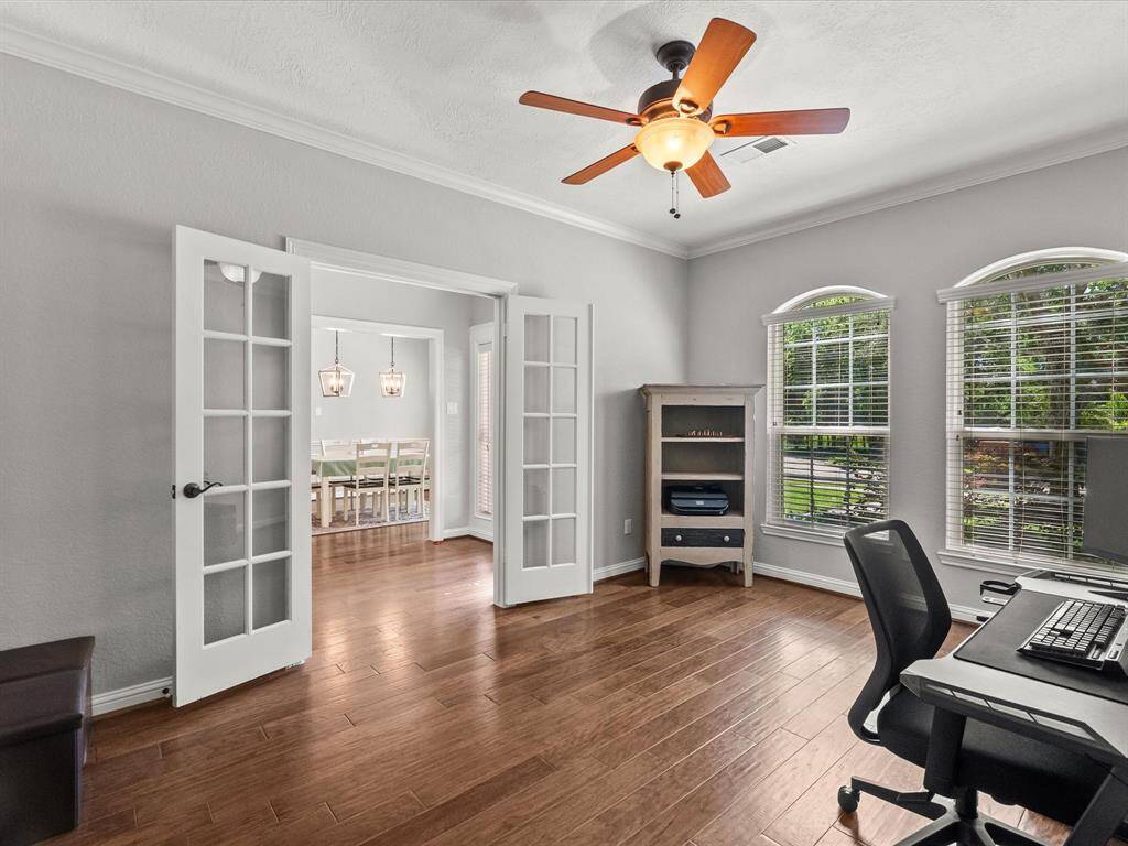 Spacious front-facing home office with French doors, ceiling fan, and large windows offering serene views and excellent natural light.