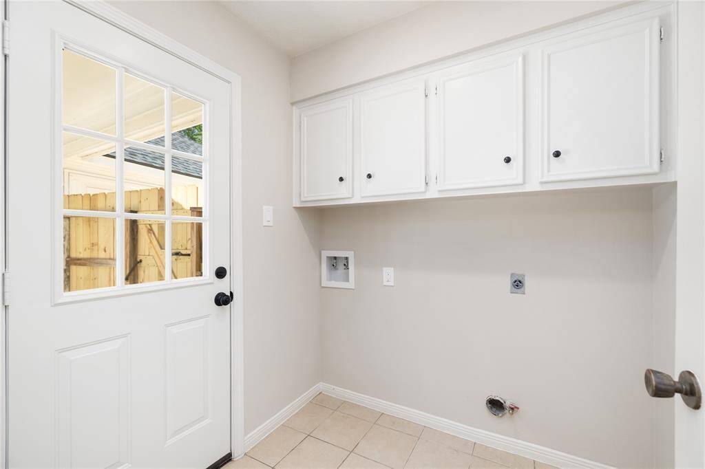 This practical laundry room is both functional and spacious, featuring ample cabinet storage and fresh paint for a clean, updated look. Serving as a mudroom, it also offers a private entrance to the backyard, providing easy access to the garage and driveway—perfect for keeping things organized and convenient.
