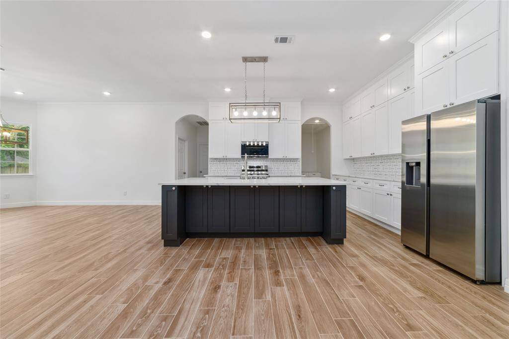 View from living room into the kitchen. Wood-look tile floors continue throughout the house. Large center island with breakfast bar.