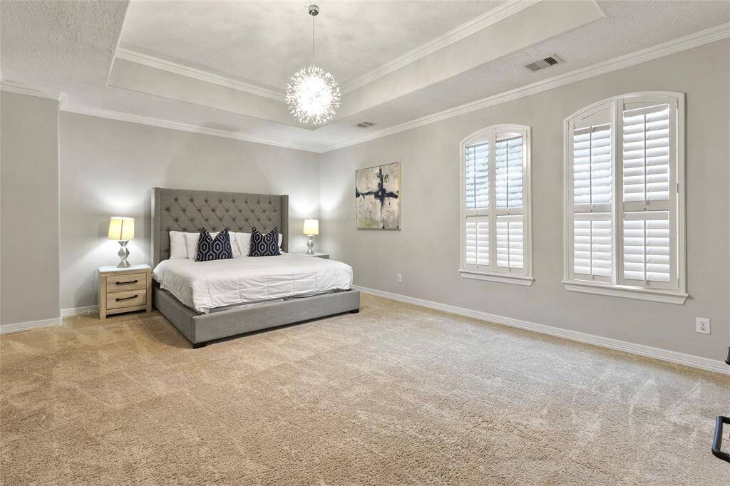 Spacious primary bedroom with neutraltones, featuring a tray ceiling and amodern chandelier. Includes a plushcarpet, large windows with shutters andplenty of room for a king sized bed andsitting area.
