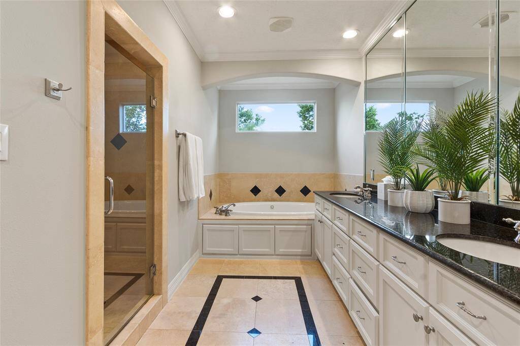 This primary bathroom features aspacious layout with a glass-enclosedshower and a large soaking tub. Itincludes dual sinks with a black granitecountertop, ample cabinetry, and largemirrors, creating a bright and elegantspace. Natural light streams in throughtwo windows above the tub.