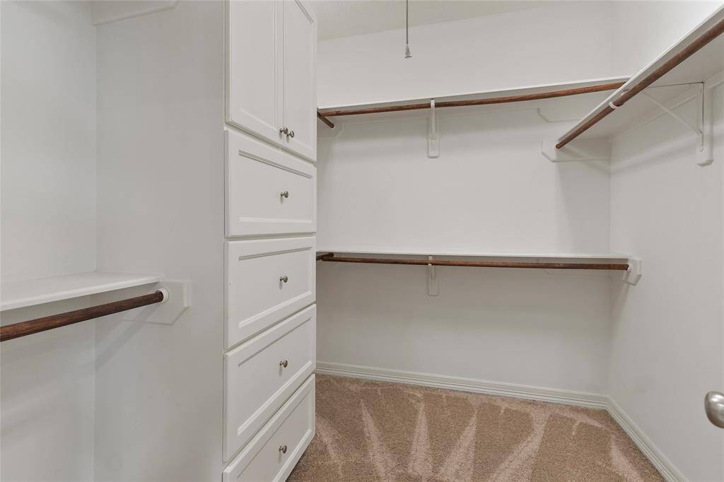 Spacious walk-in closet with ampleshelving and hanging space, featuringbuilt-in drawers and neutral carpeting.Ideal for organized storage.