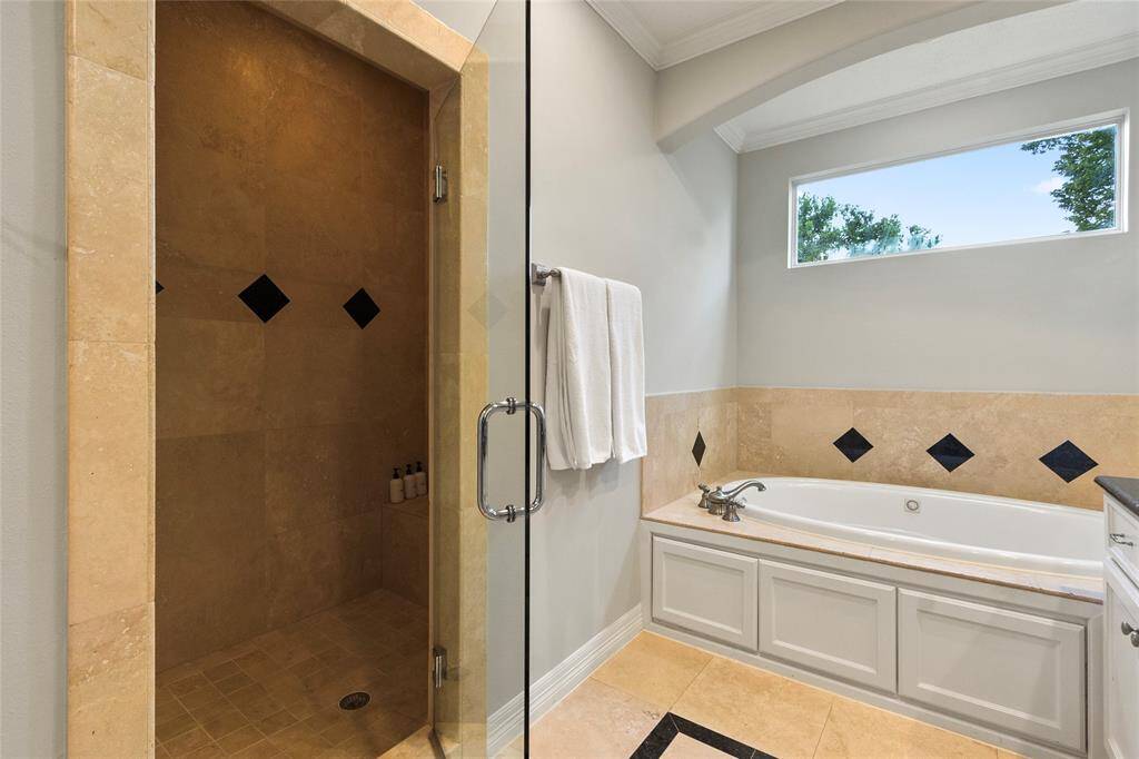 This bathroom features a spaciouswalk-in shower with glass door andelegant tiling, alongside a luxuriousbuilt-in bathtub with black diamondaccents. A large window providesnatural light.