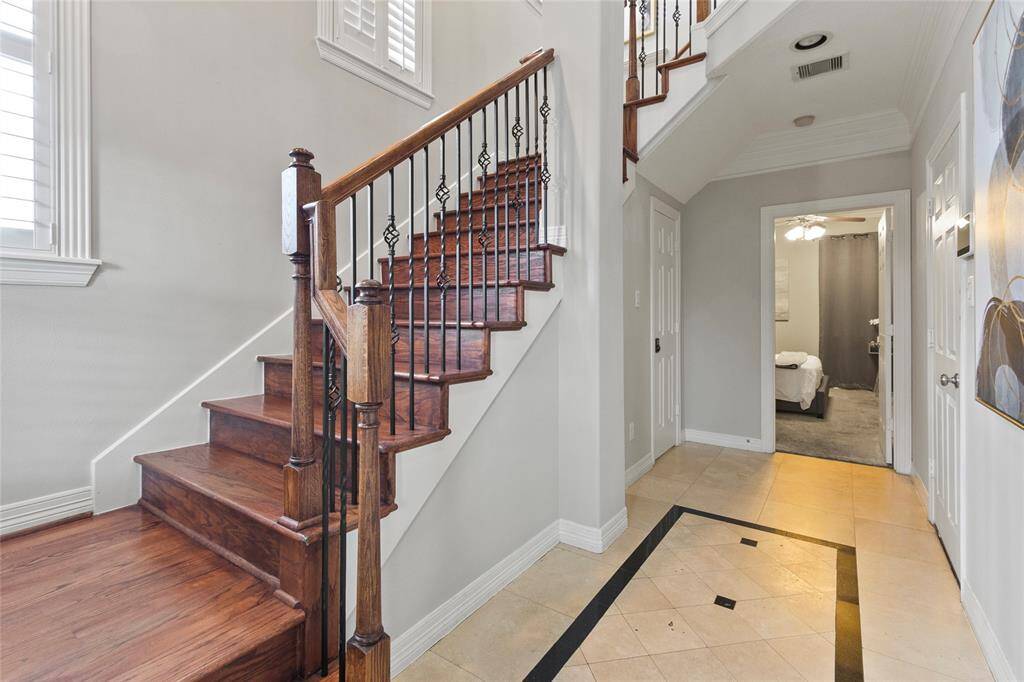 This photo showcases a bright entrywaywith elegant wooden stairs featuringwrought iron balusters. The spaceincorporates tiled flooring with adecorative inlay and leads into a cozycarpeted room, offering both style andfunctionality for a welcoming homeatmosphere.