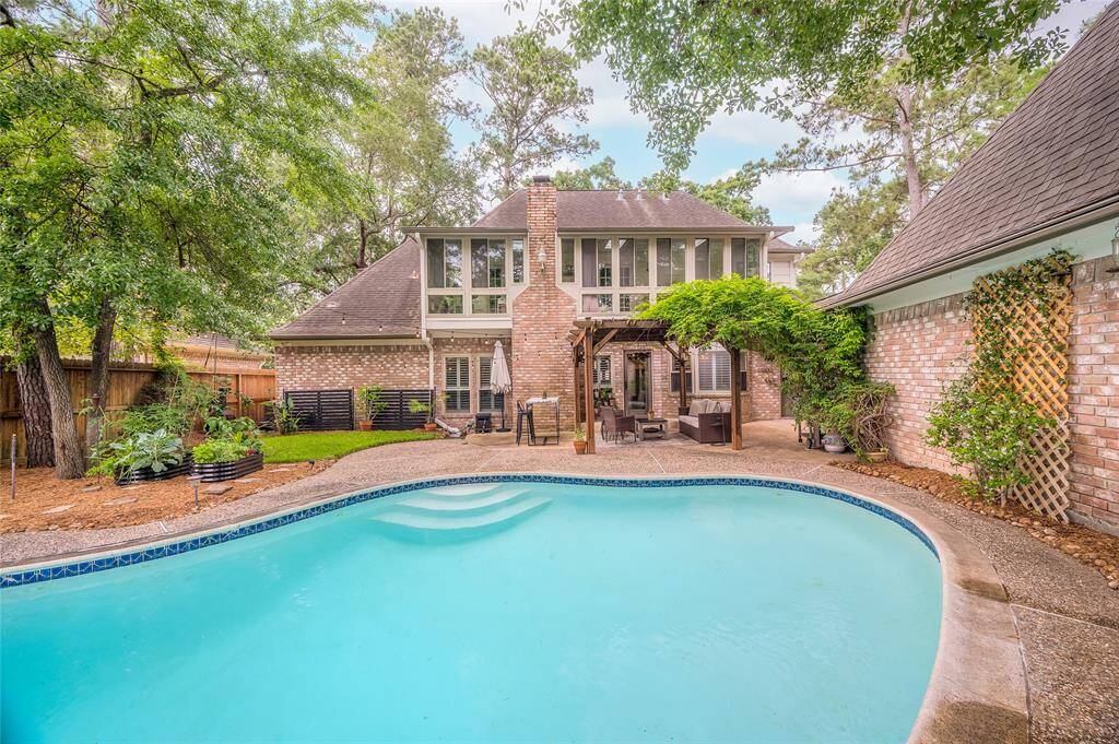 This inviting home features a spacious backyard with a swimming pool, surrounded by lush greenery. A charming brick exterior and a cozy patio with a pergola offer an ideal space for outdoor relaxation and entertainment.