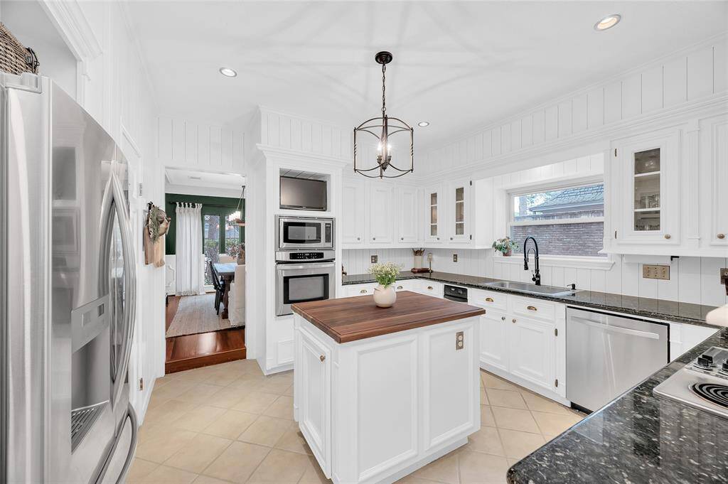 This bright kitchen features white cabinetry, granite countertops, and a central island with a wood top. Stainless steel appliances, including a built-in microwave and oven, enhance functionality. A large window above the sink adds natural light, and a stylish pendant light completes the look.