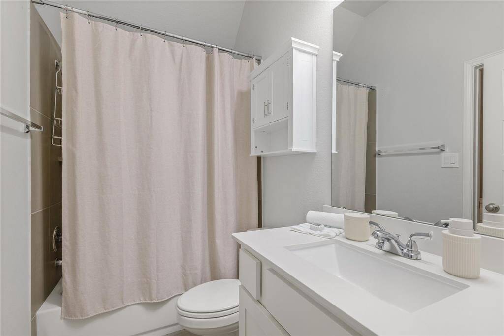 This bathroom features a clean, modern design with a white vanity, chrome faucet, and ample mirror space. It includes a bathtub with a neutral shower curtain and convenient storage with a wall-mounted cabinet. The overall look is bright and inviting.