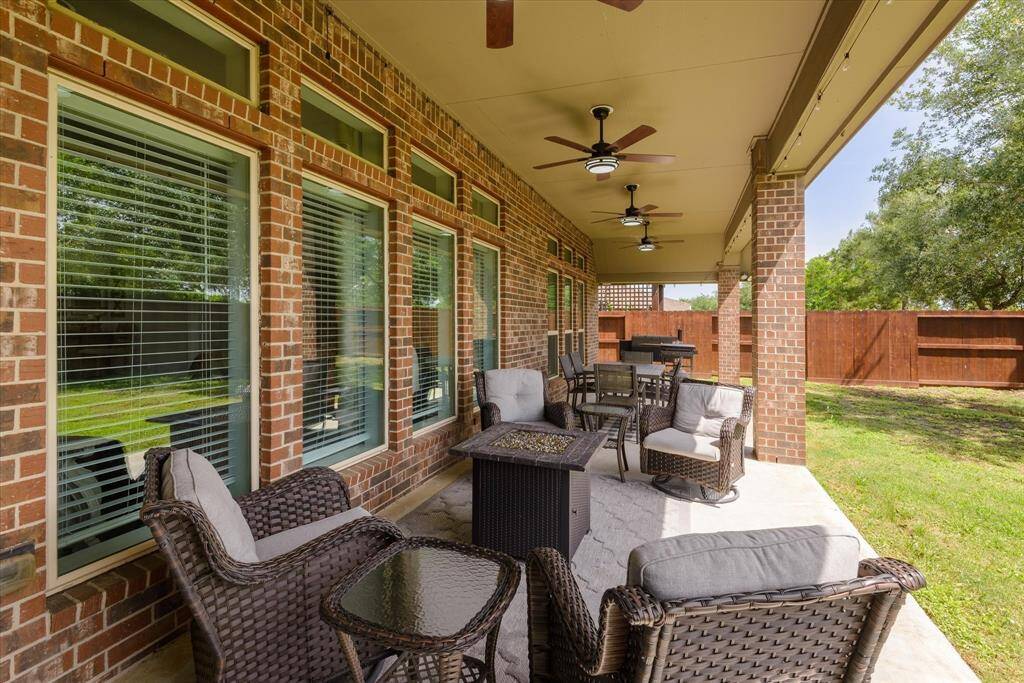 This photo showcases a spacious covered patio with ceiling fans, perfect for outdoor dining and relaxation. It's adjacent to a well-maintained lawn, enclosed by a wooden privacy fence, ideal for entertaining and enjoying the outdoors.