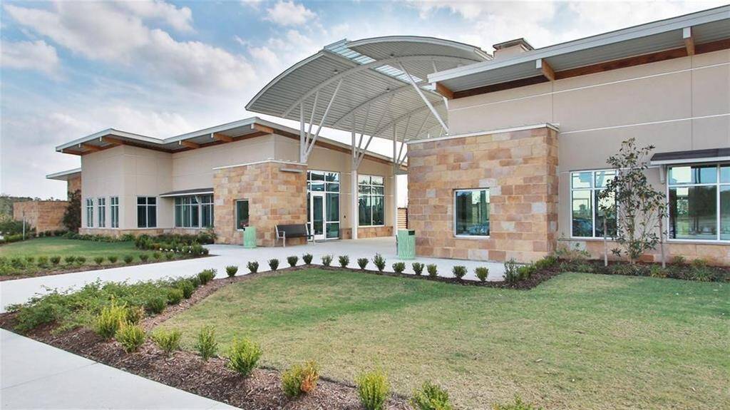 This photo showcases a modern community center with a blend of stone and glass elements, featuring an eye-catching curved roof and well-maintained landscaping. Ideal for those seeking contemporary architectural style.
