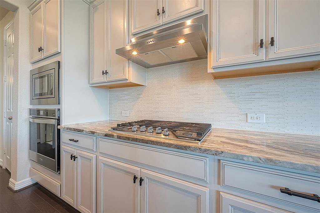The kitchen is a symphony of modern design and practical functionality, with granite countertops, gas cooktop an gleaming stainless-steel appliances that catch the light.
