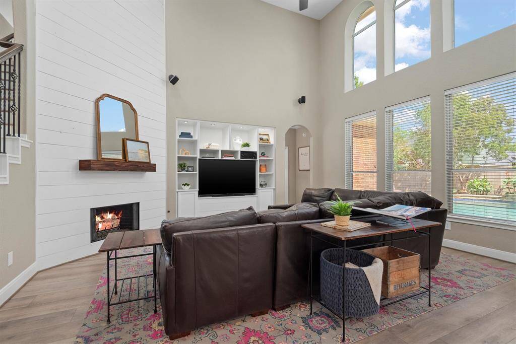 The cozy fireplace with white shiplap accent wall and wooden mantle creates a charming focal point. The built-in entertainment center is framed by recessed lighting and open shelving for both function and display.
