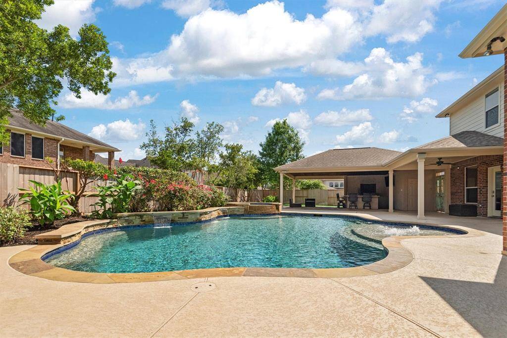 Fantastic backyard featuring a beautifully designed pool with a stone waterfall feature, surrounded by lush landscaping. Adjacent to the pool is an oversized covered patio area, perfect for outdoor entertaining and relaxation.