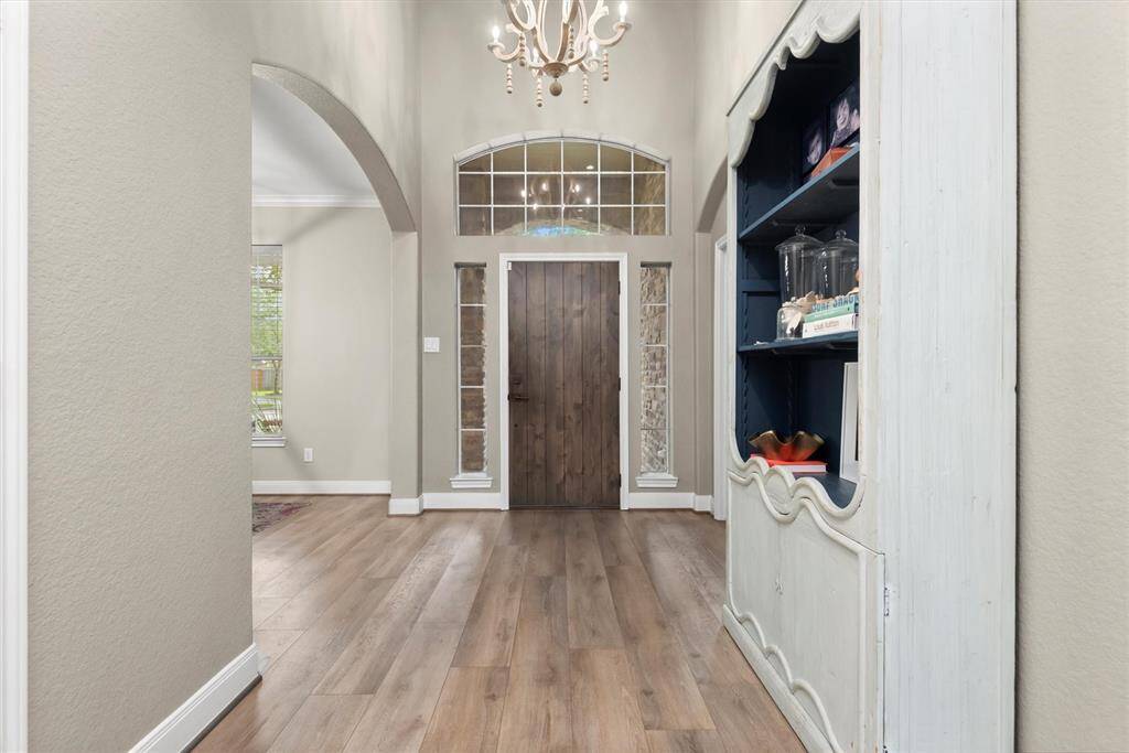 The foyer features a wooden door with decorative glass panels, high ceiling, and a stylish chandelier, creating a welcoming and elegant atmosphere.