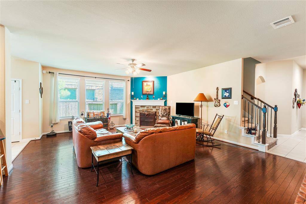 Roomy living room features warm wood floors, a custom stone wood-burning fireplace with a rich wooden mantel, and an abundance of natural light.