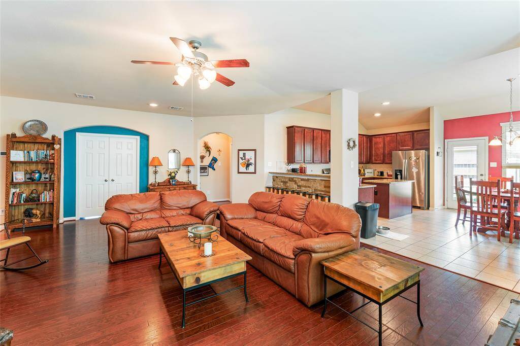 Roomy living room features warm wood floors, a custom stone wood-burning fireplace with a rich wooden mantel, and an abundance of natural light.