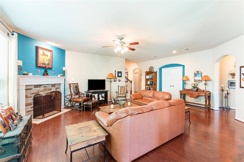 Roomy living room features warm wood floors, a custom stone wood-burning fireplace with a rich wooden mantel, and an abundance of natural light.