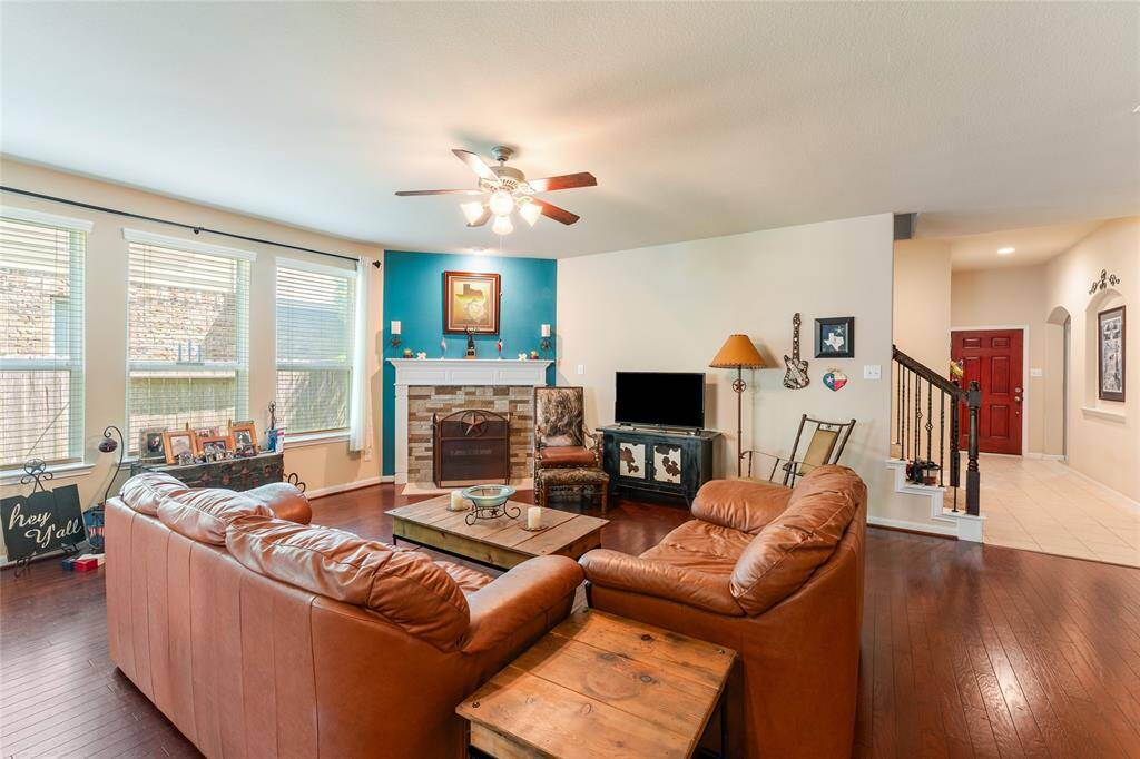 Roomy living room features warm wood floors, a custom stone wood-burning fireplace with a rich wooden mantel, and an abundance of natural light.
