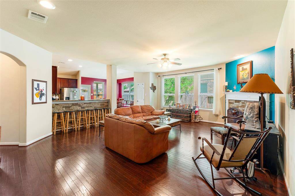Roomy living room with rich wood floors, a custom stone fireplace, and abundant natural light—seamlessly open to a kitchen bar that comfortably seats six.