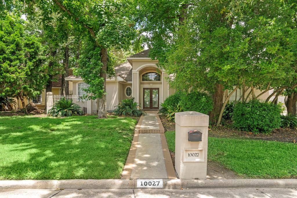 Charming home with a welcoming front entrance, surrounded by lush greenery. A concrete path leads from the street to the doorway, framed by mature trees and a well-maintained lawn. The address is prominently displayed on a mailbox at the curb.
