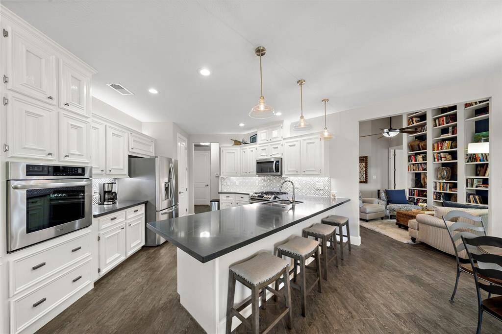 This photo showcases a modern, open-concept kitchen with sleek stainless steel appliances, a large island with seating, and elegant pendant lighting. The space flows into a cozy living area with built-in bookshelves, creating a warm and inviting atmosphere.