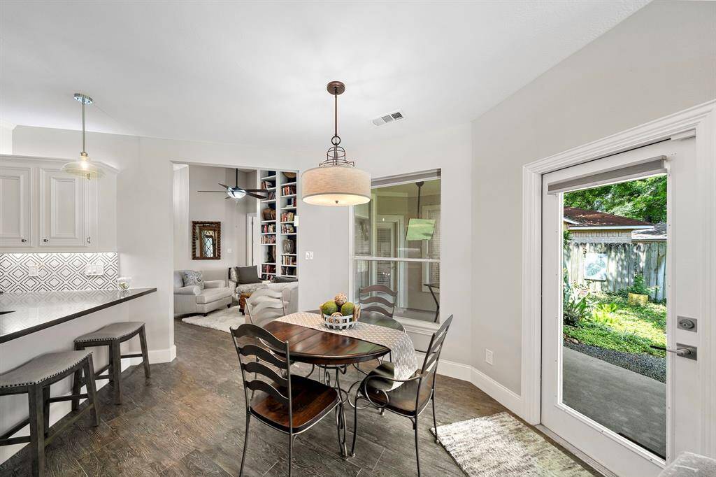 This inviting home features an open-concept kitchen and dining area with modern finishes and bar seating. The adjacent living room offers a cozy space with built-in shelving. Large windows and a glass door provide ample natural light and access to a lush backyard.