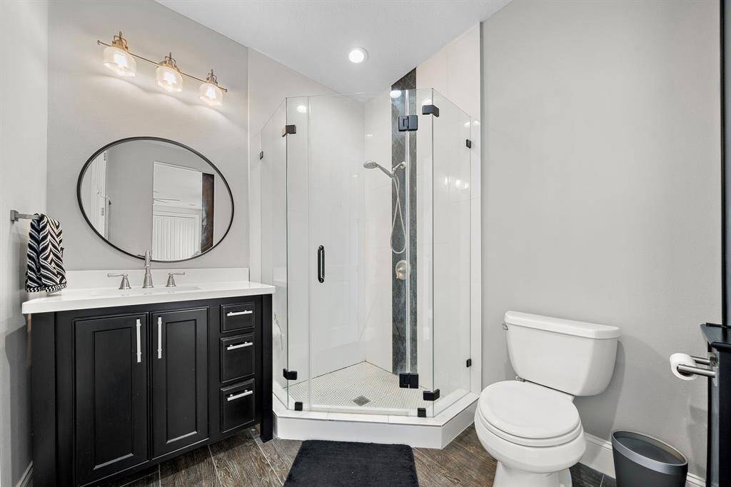 This bathroom features a modern design with a sleek black vanity, a round mirror, and a glass-enclosed corner shower. It has elegant lighting and neutral tones for a contemporary feel.
