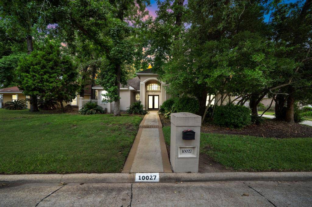 Escape into a cozy backyard with lush greenery and mature trees surrounding a single-story home. The house features a covered patio area, perfect for outdoor dining and relaxation, and a well-maintained lawn. The evening lighting adds a warm, inviting ambiance.