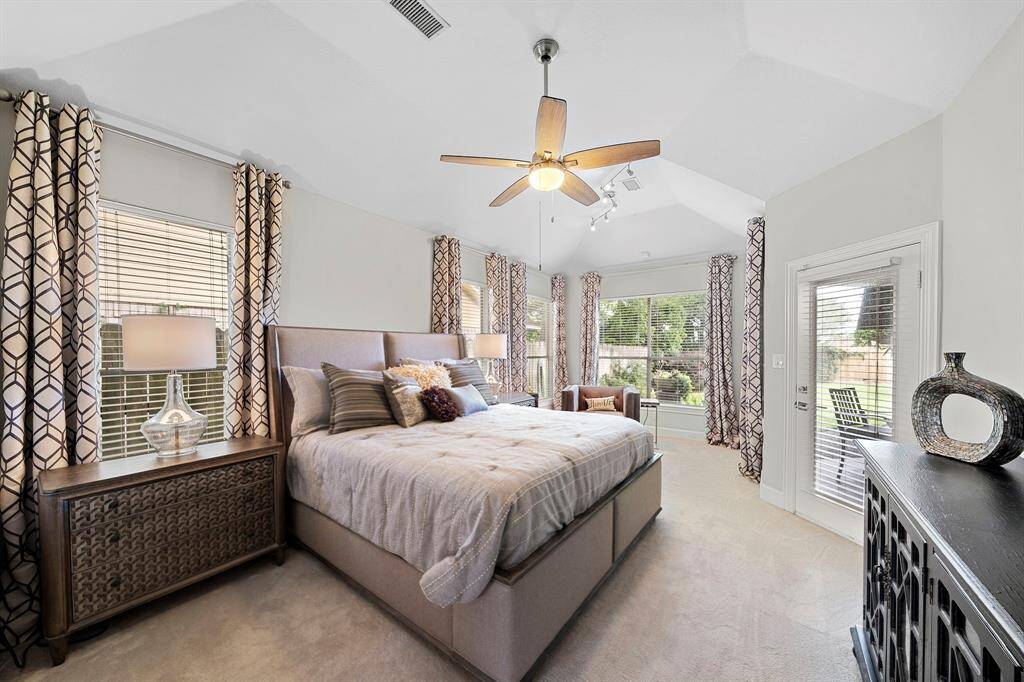 Spacious and bright bedroom with large windows, patterned curtains, and neutral tones. It features a ceiling fan, comfortable bed, and access to a patio, offering a cozy and inviting atmosphere.