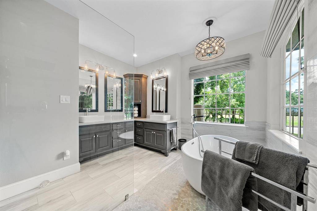 This elegant bathroom features a spacious design with a freestanding tub, large window for natural light, double vanity with dark cabinetry, modern fixtures, and a luxurious glass shower. Perfect for relaxation and style.