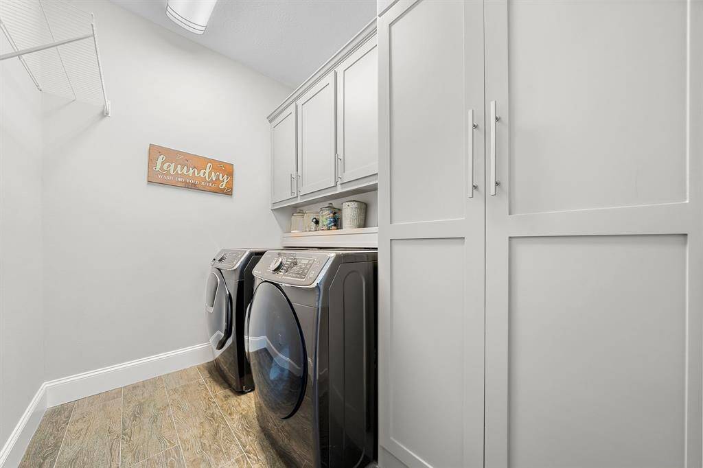 This photo showcases a modern laundry room with sleek cabinets, a washer and dryer set, and ample storage space. The room is bright and organized, featuring a decorative "Laundry" sign and wood-look flooring.