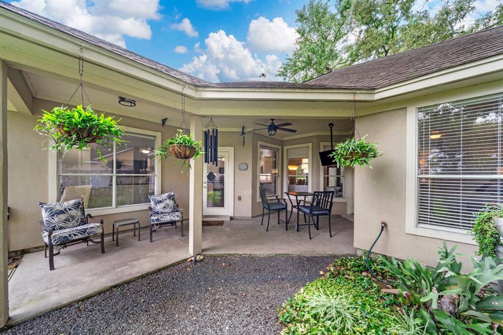 This inviting backyard patio features a covered seating area with outdoor furniture, hanging plants, and a ceiling fan, offering a cozy space for relaxation and entertaining.