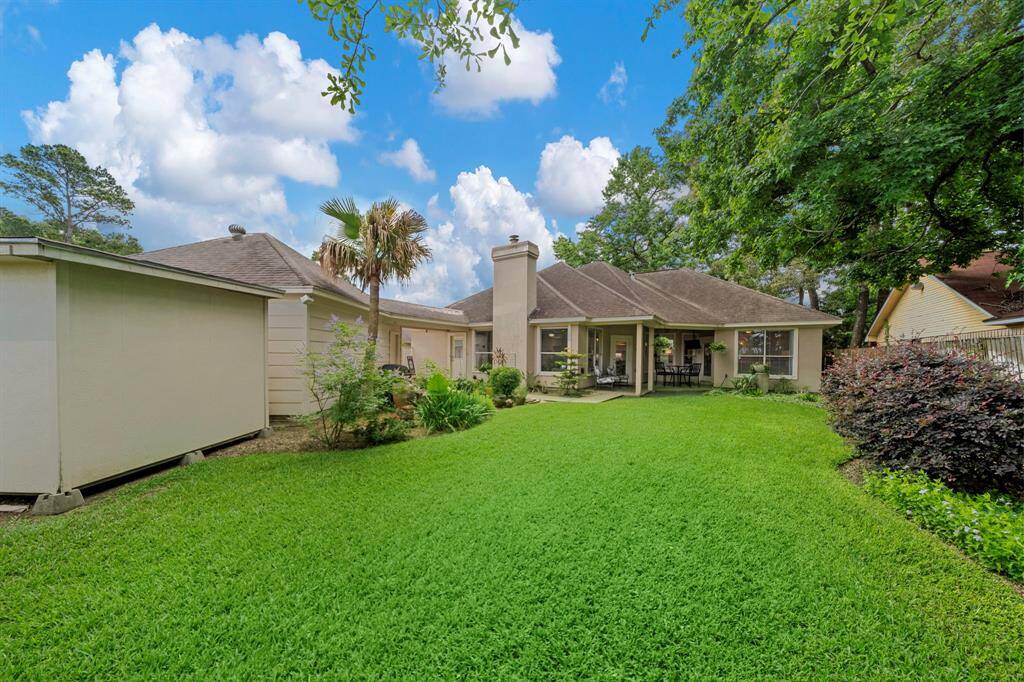 This photo showcases a charming backyard with a well-maintained lawn, lush greenery, and a spacious patio area attached to a single-story home, perfect for outdoor relaxation and entertaining.