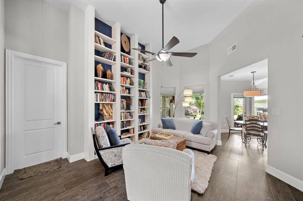 This cozy living room features a high ceiling and a stylish ceiling fan. A built-in bookshelf adds character, while natural light streams in through large windows. The space flows seamlessly into a dining area, perfect for entertaining.