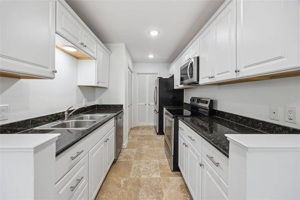Modern kitchen with sleek black granite countertops, white cabinetry, and stainless steel appliances. Bright, neutral tones and ample natural light from a large window from dining room that creates an inviting space leading to living room