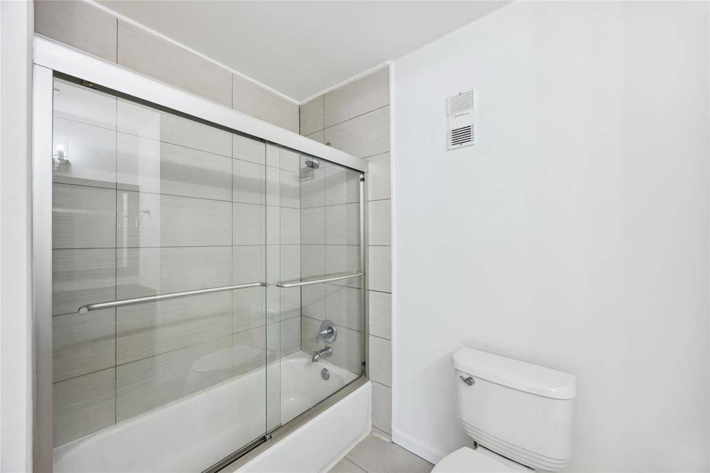Bathroom featuring a tub/shower combo enclosed with sleek sliding glass doors, a functional and stylish upgrade