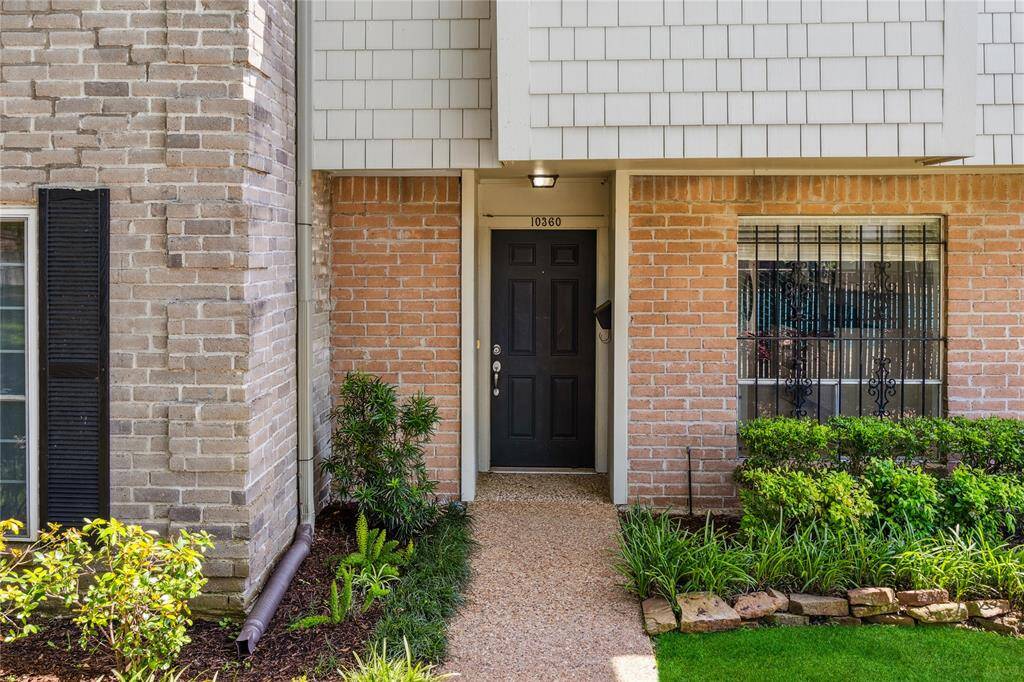 Charming front entrance with a black door, surrounded by brick and siding. Well-maintained landscaping includes lush bushes and small plants, adding curb appeal.