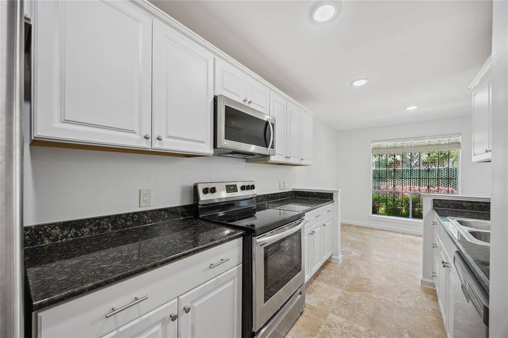 Modern kitchen with sleek black granite countertops, white cabinetry, and stainless steel appliances. Bright, neutral tones and ample natural light from a large window from dining room that creates an inviting space.