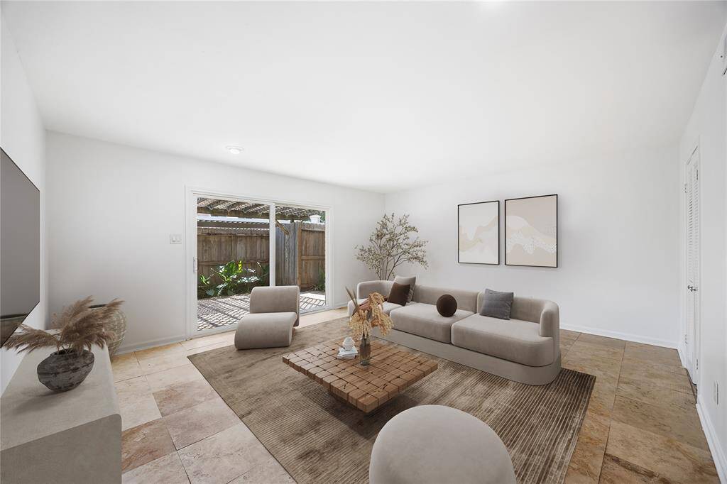 This bright living room features a modern, neutral design with large sliding glass doors that lead to a cozy outdoor space, enhancing natural light.