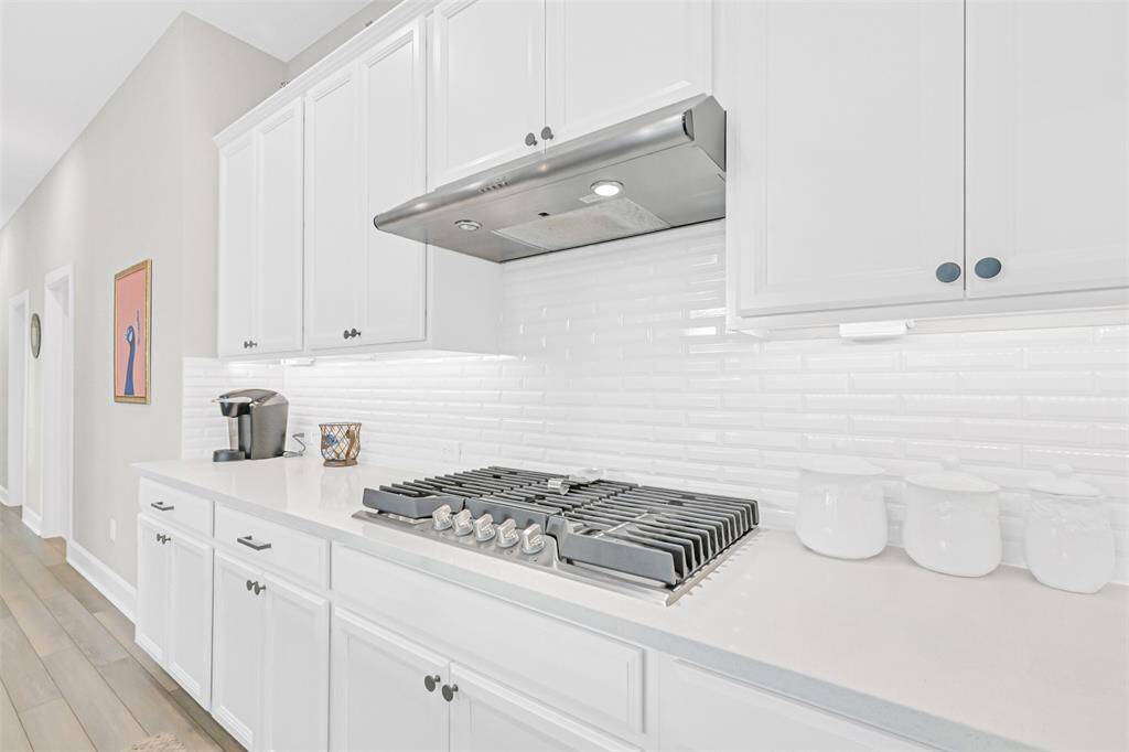 A chef’s dream, the sleek gas cooktop is set against a modern subway tile backsplash, surrounded by abundant counter space and white shaker cabinets for a clean, modern finish.
