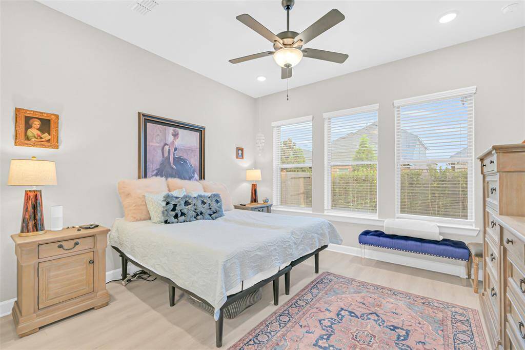Retreat to the serene primary bedroom, where soft natural light pours through three large windows, highlighting designer touches and warm wood accents.